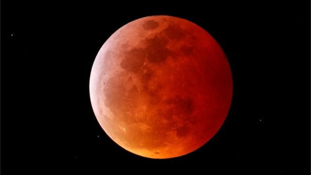 Foto de uma lua vermelha no cél estrelado.